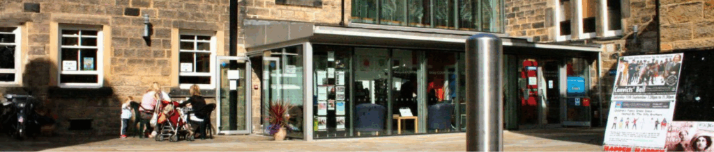 Otley Courthouse – Venue image showing a modern glass extension connecting two parts of a historic stone building with slate roofs. Located in Otley, West Yorkshire, the venue features traditional windows, a paved courtyard, and outdoor seating, blending contemporary design with heritage architecture.